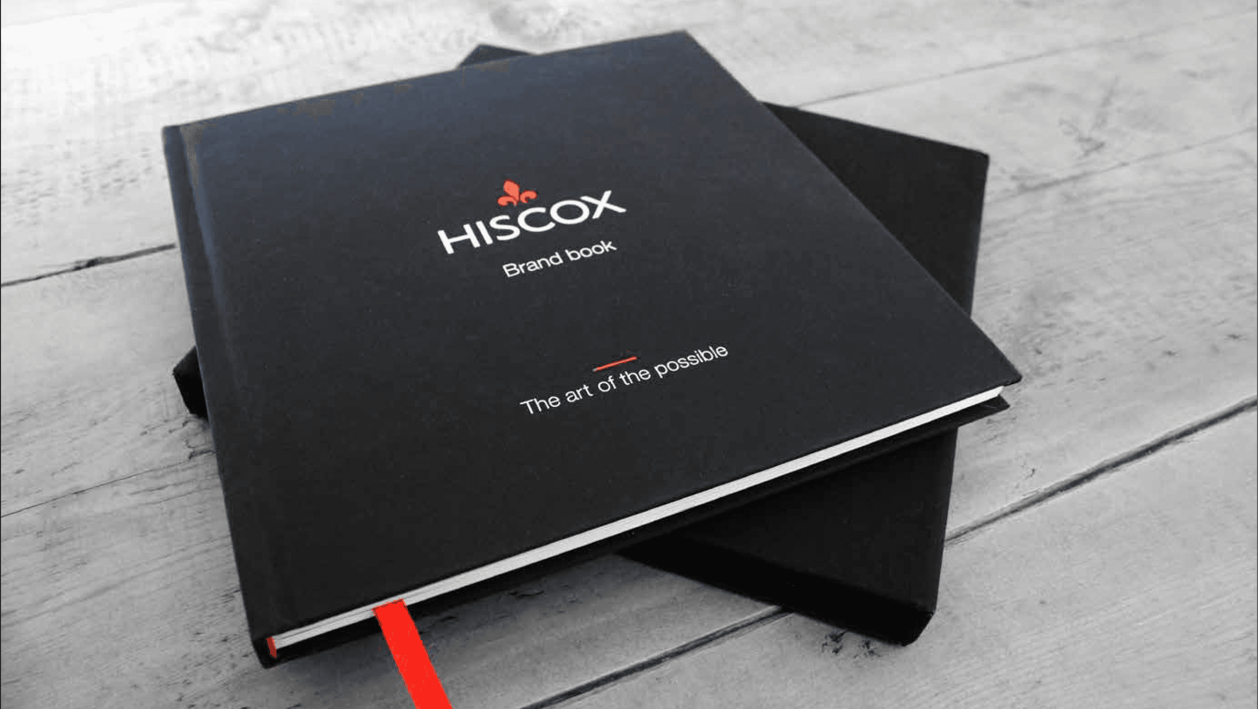 Black Hiscox brand book titled 'The art of the possible' stacked on a wooden surface.